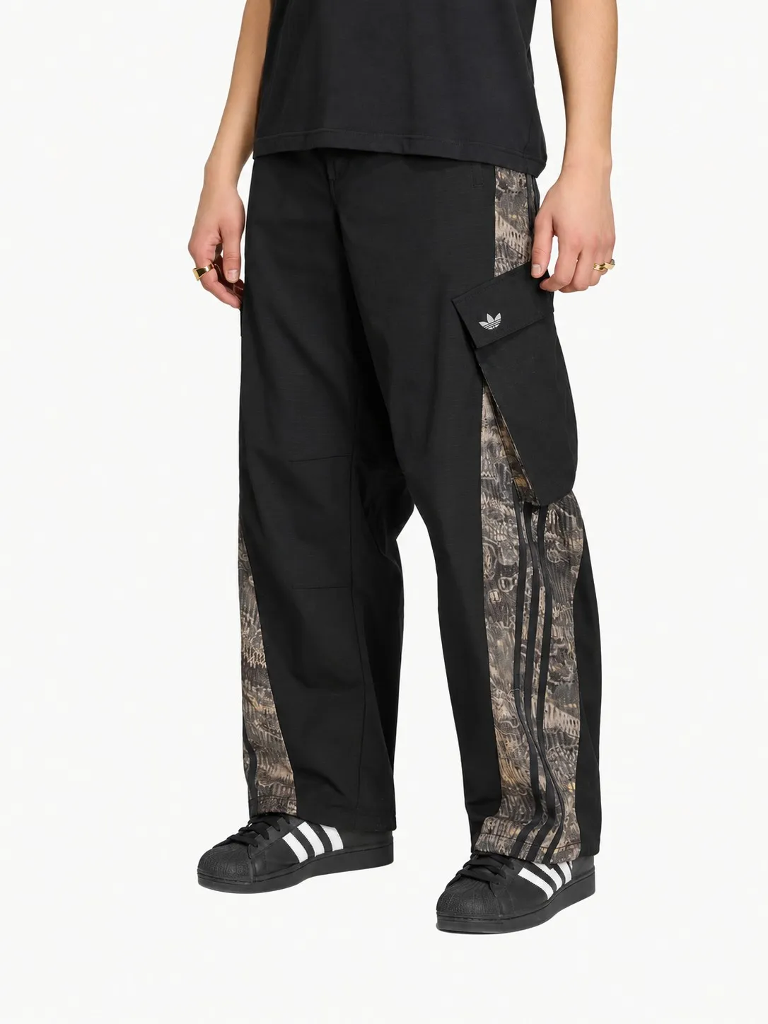 Pantalón cargo Adidas negro puesto, plano de la cintura para abajo de un modelo con camiseta negra y tenis Superstar negros