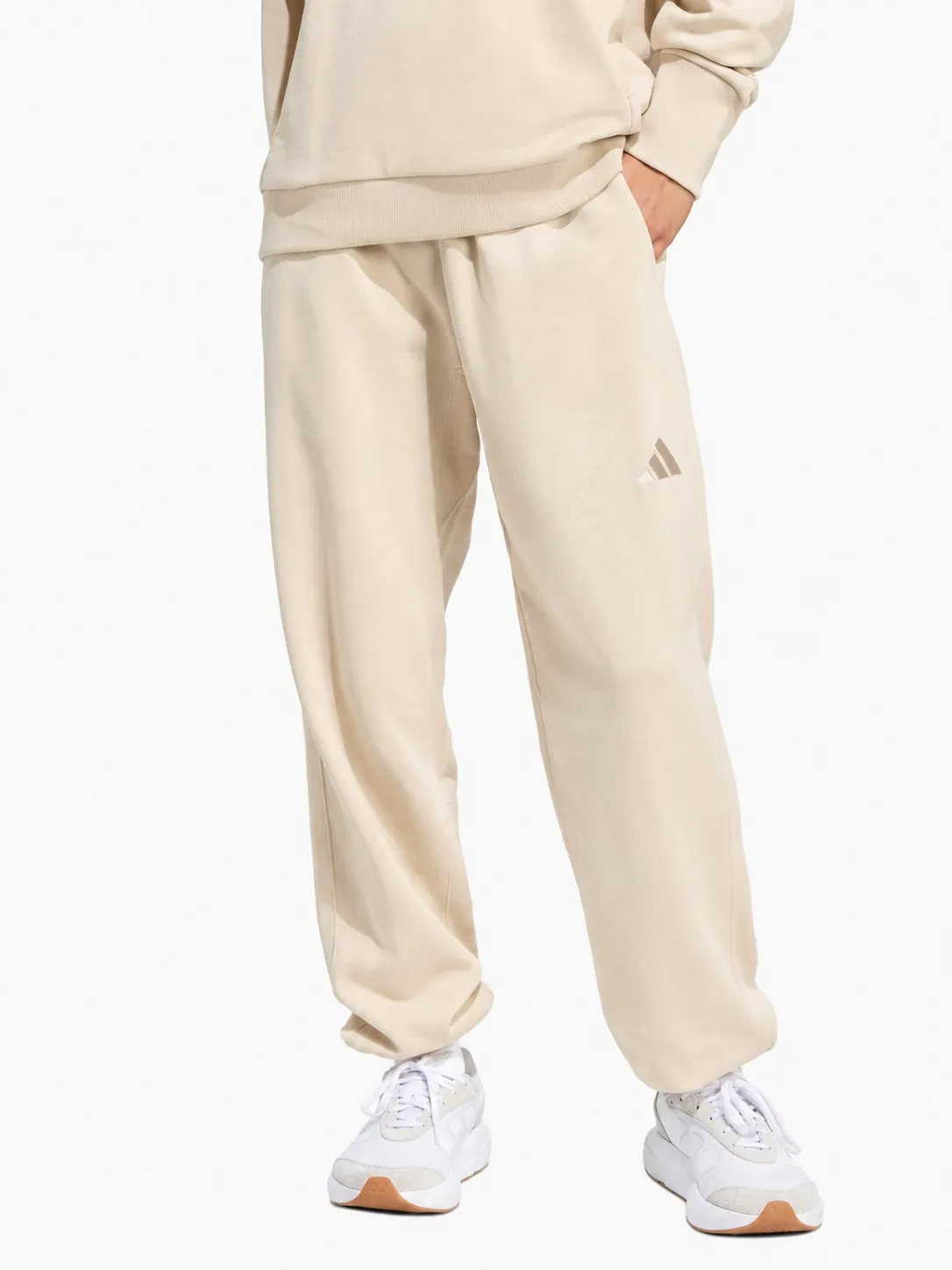 Pantalón Adidas beige puesto, plano de la cintura para abajo de una persona que lo lleva con buzo a juego y tenis blancos