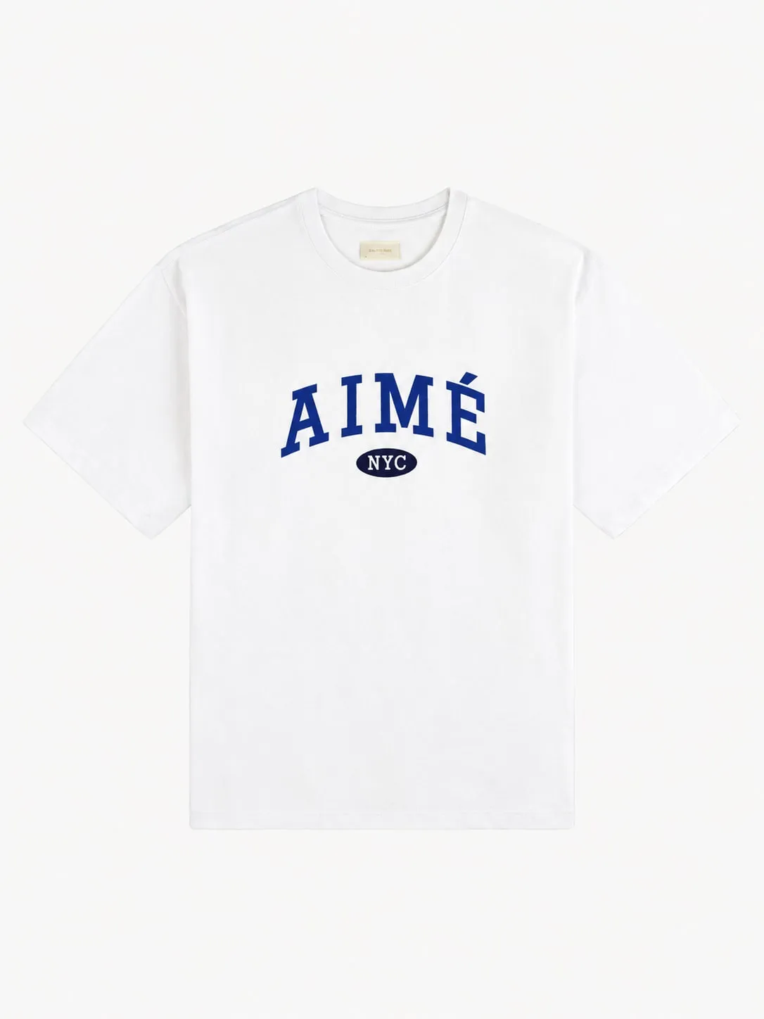 Camiseta Aimé Leon Dore blanca, vista frontal de la prenda sola con la palabra AIMÉ en letra universitaria azul arqueada y NYC dentro de un óvalo azul marino debajo