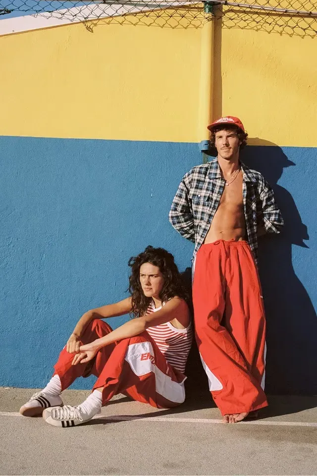 Pareja con pantalones de paracaídas rojos contra una pared azul y amarilla