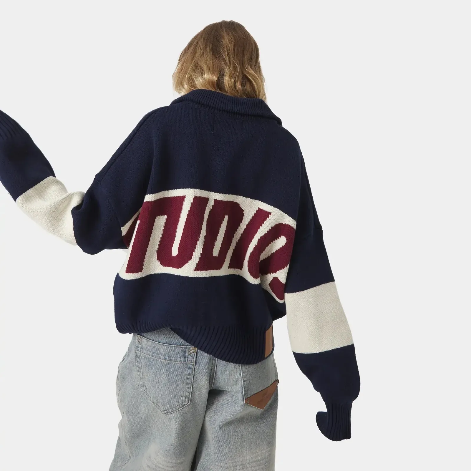 Chica de espaldas con un jersey azul marino con Studios tejido en granate y blanco