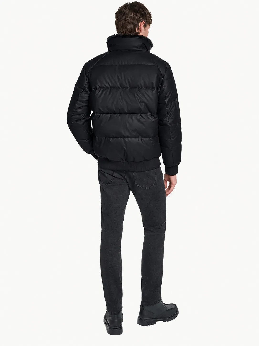 Chaqueta bomber Karl Lagerfeld negra puesta, vista de espalda de cuerpo entero de un modelo con jean negro y botas