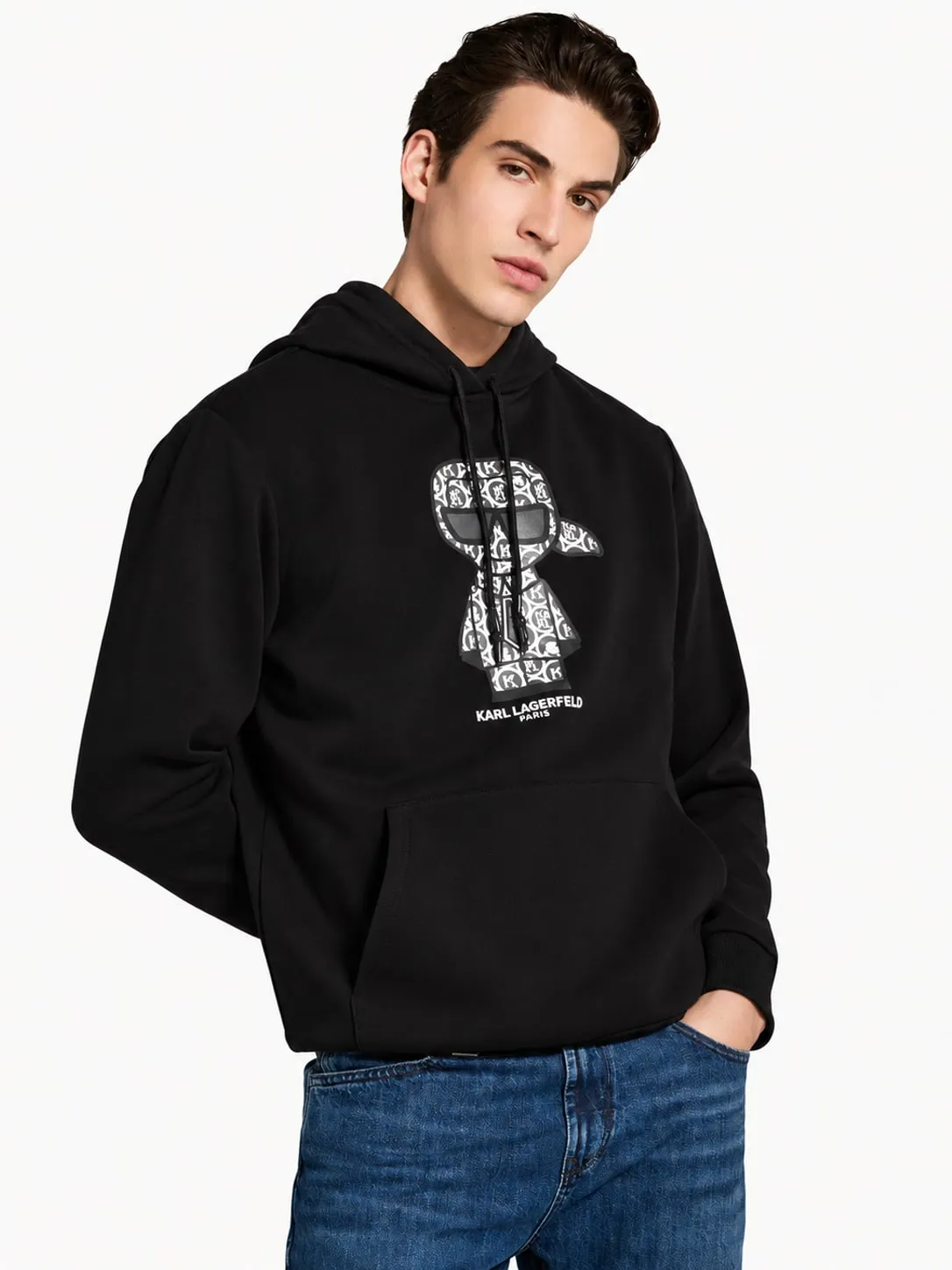 Hoodie Karl Lagerfeld negro puesto, plano medio de un modelo que lo lleva con jeans azules y una mano en el bolsillo