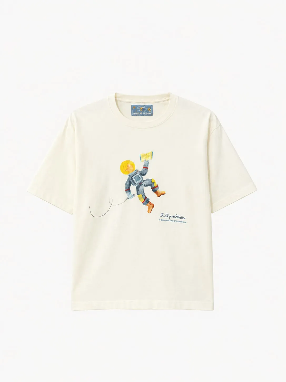 Camiseta KidSuper Studios color crudo, vista frontal de la prenda sola con un astronauta en acuarela azul y amarillo flotando con un libro abierto y la firma de la marca en azul a la derecha