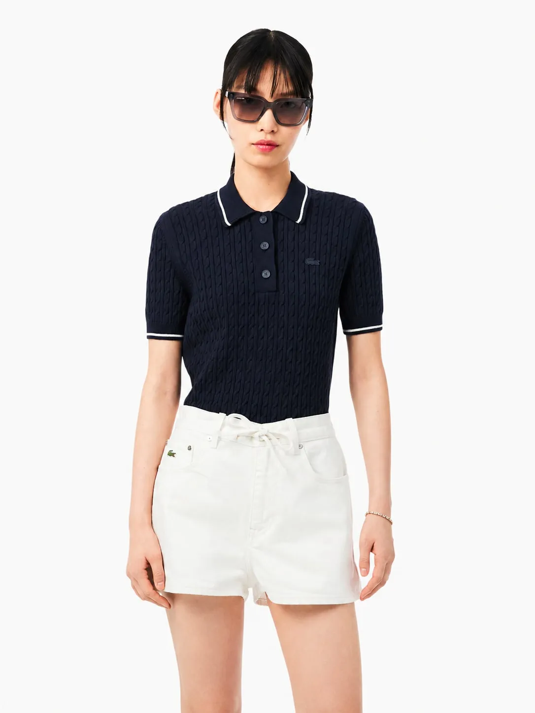 Polo Lacoste de punto trenzado azul marino puesto, plano medio de una modelo que lo lleva con shorts vaqueros blancos