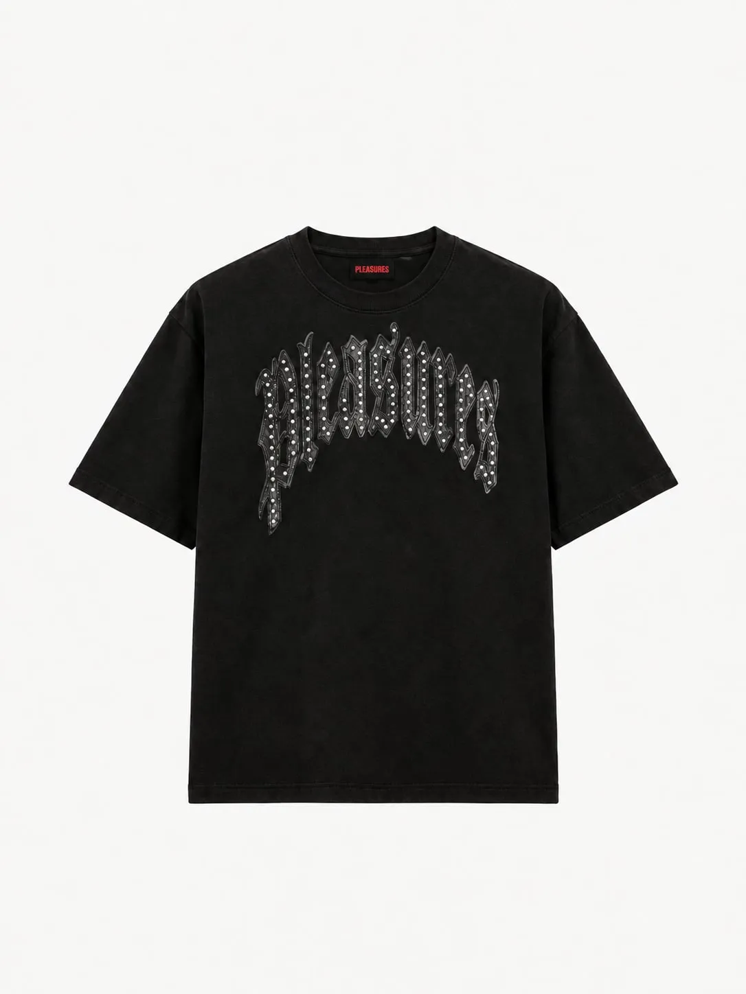 Camiseta Pleasures negra desgastada, vista frontal de la prenda sola con el logo Pleasures en letra gótica arqueada, aplicado en cuero negro con remaches plateados, y la etiqueta roja en el cuello